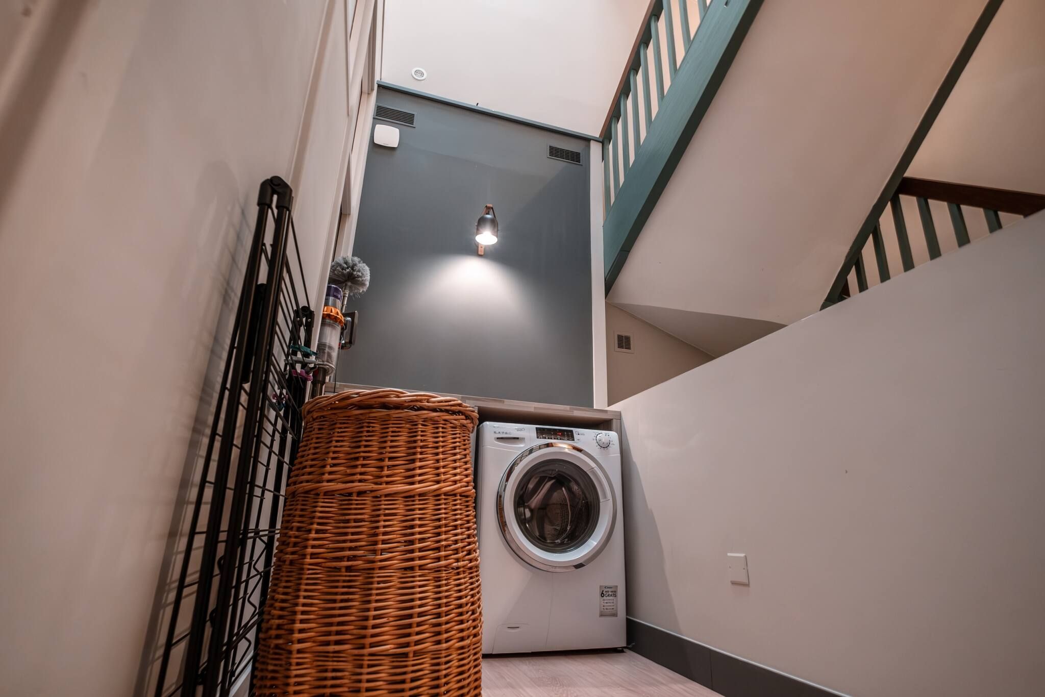 A laundry room with a washing machine, a wicker basket, and a staircase.