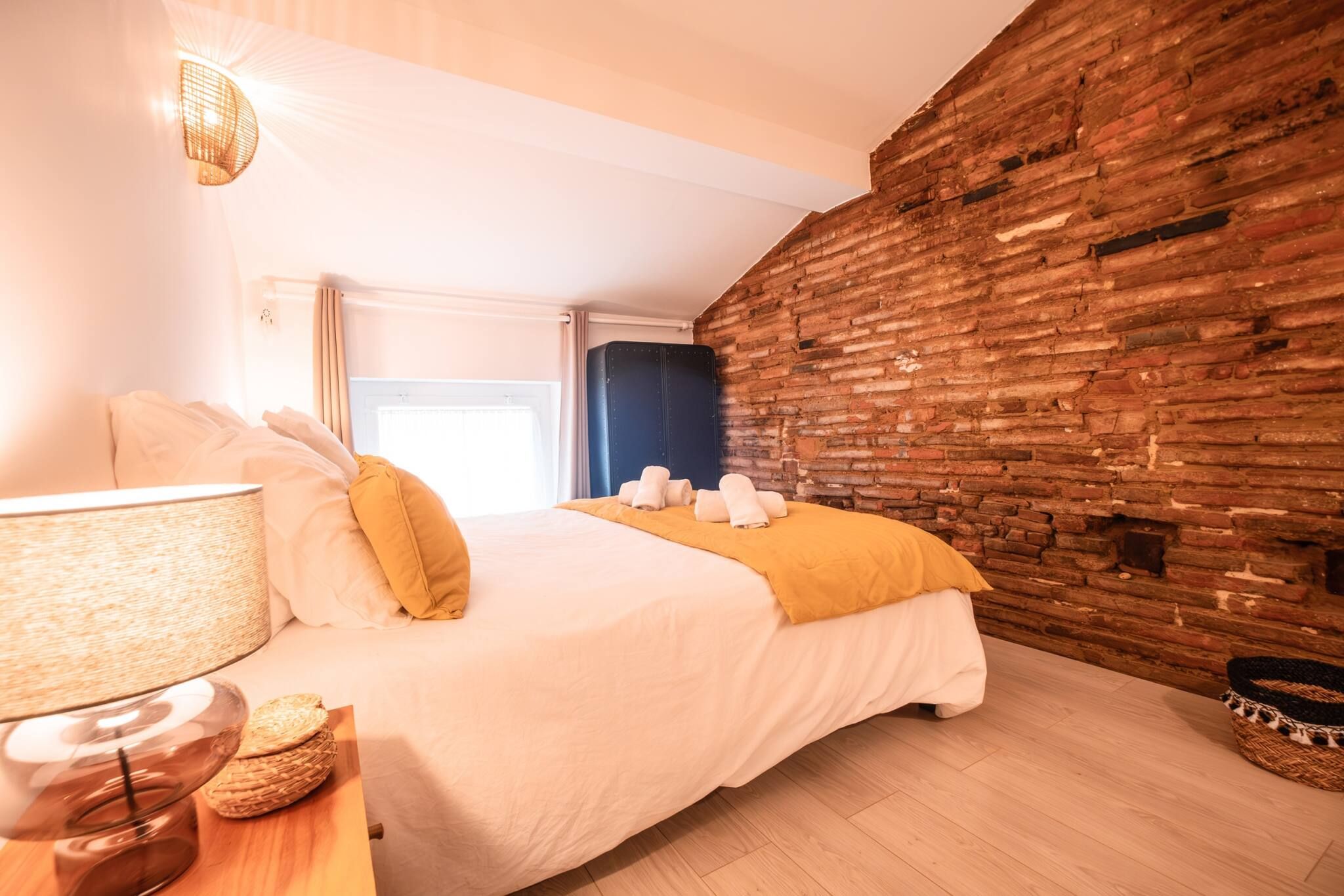 Een hotelkamer met een bed, een lamp, een houten nachtkastje en een bakstenen muur.