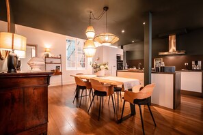 Een moderne keuken met houten vloer, een eettafel met stoelen, hangende verlichting en een inbouw kookeiland.