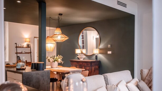 A modern living room with a sofa, a dining table, and a kitchen area in the background.
