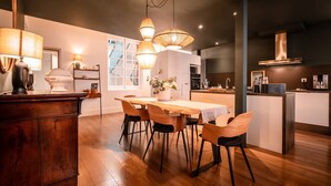 A modern kitchen with wooden flooring, a dining table with chairs, pendant lighting, and a built-in island with a stove.