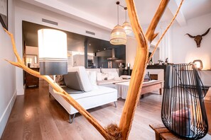 A modern living room with a white sofa, a dining area with a black chair, and a kitchen in the background. - Le Duplex - Air con - Parking - WiFi (Montauban)
