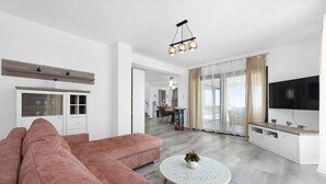 A modern living room with a large pink sectional sofa, a round coffee table with a decorative centerpiece, and a flat-screen TV mounted on the wall. - Enchanting Villa North with Pool and Jacuzzi (Krnica)