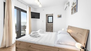 A modern bedroom with a wooden bed, a flat-screen TV, a ceiling light, and a view through a large window. - Enchanting Villa North with Pool and Jacuzzi (Krnica)