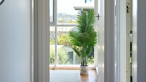Een hal met een groot raam dat uitkomt op een balkon, een potplant en een houten vloer.