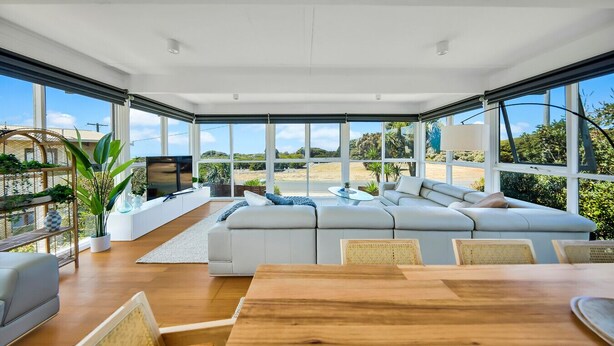 Een moderne woonkamer met een grote hoekbank, een houten eettafel en een televisie.