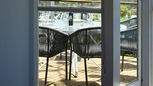 Een overdekt terras met eettafel en stoelen, een waterfles en uitzicht op een woonwijk.