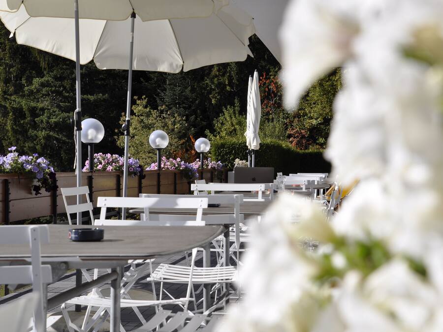 Outdoor tables and chairs with umbrellas, surrounded by flowers and greenery.