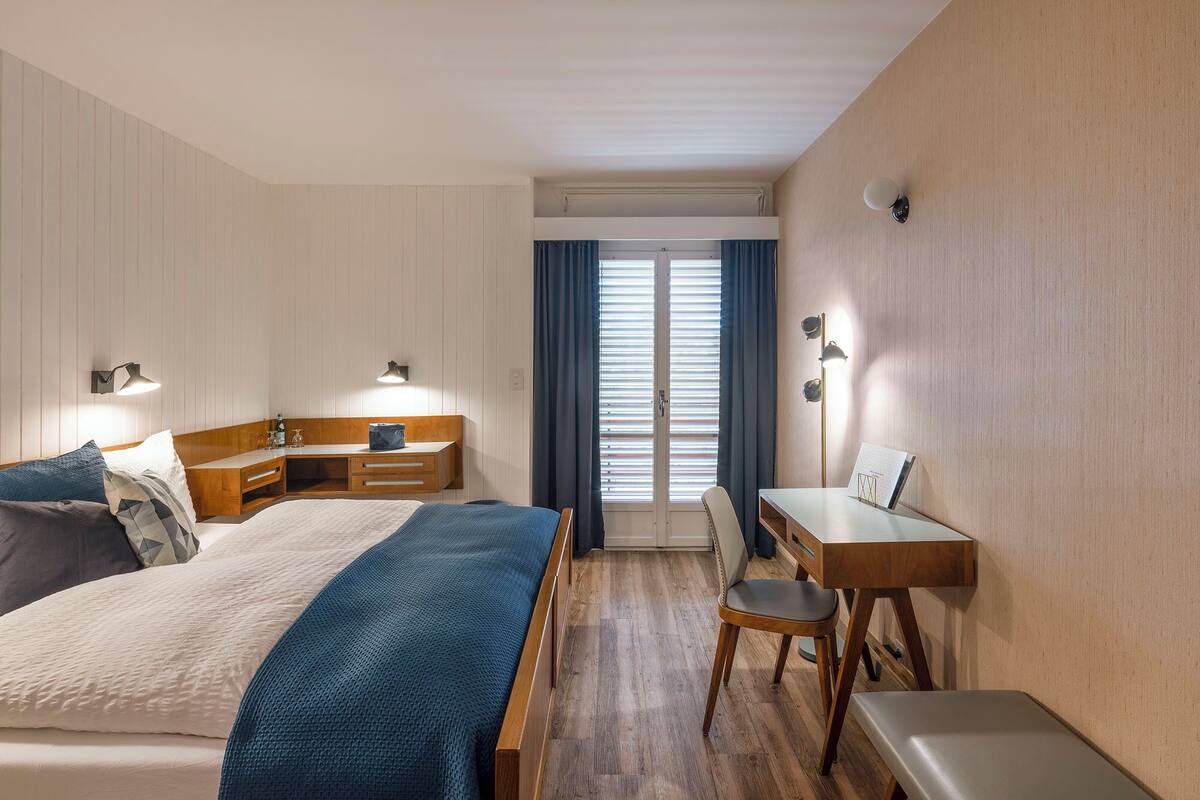 Une chambre d’hôtel avec un lit, une table de chevet, un bureau, une chaise et une vue par la fenêtre.
