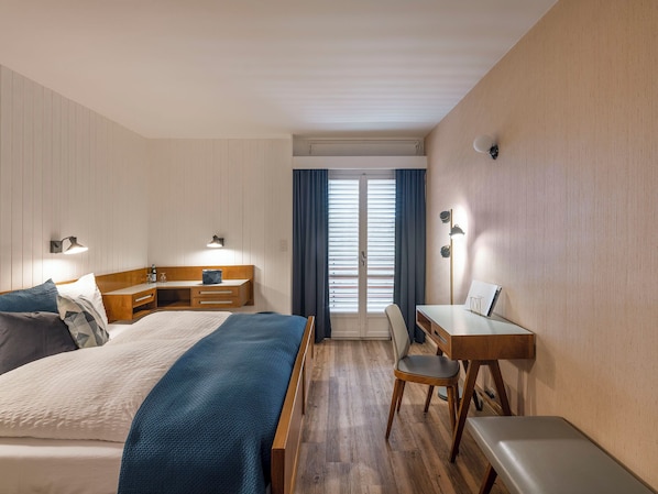 Una habitación de hotel con cama, mesita de noche, escritorio, silla y vistas a la ventana.
