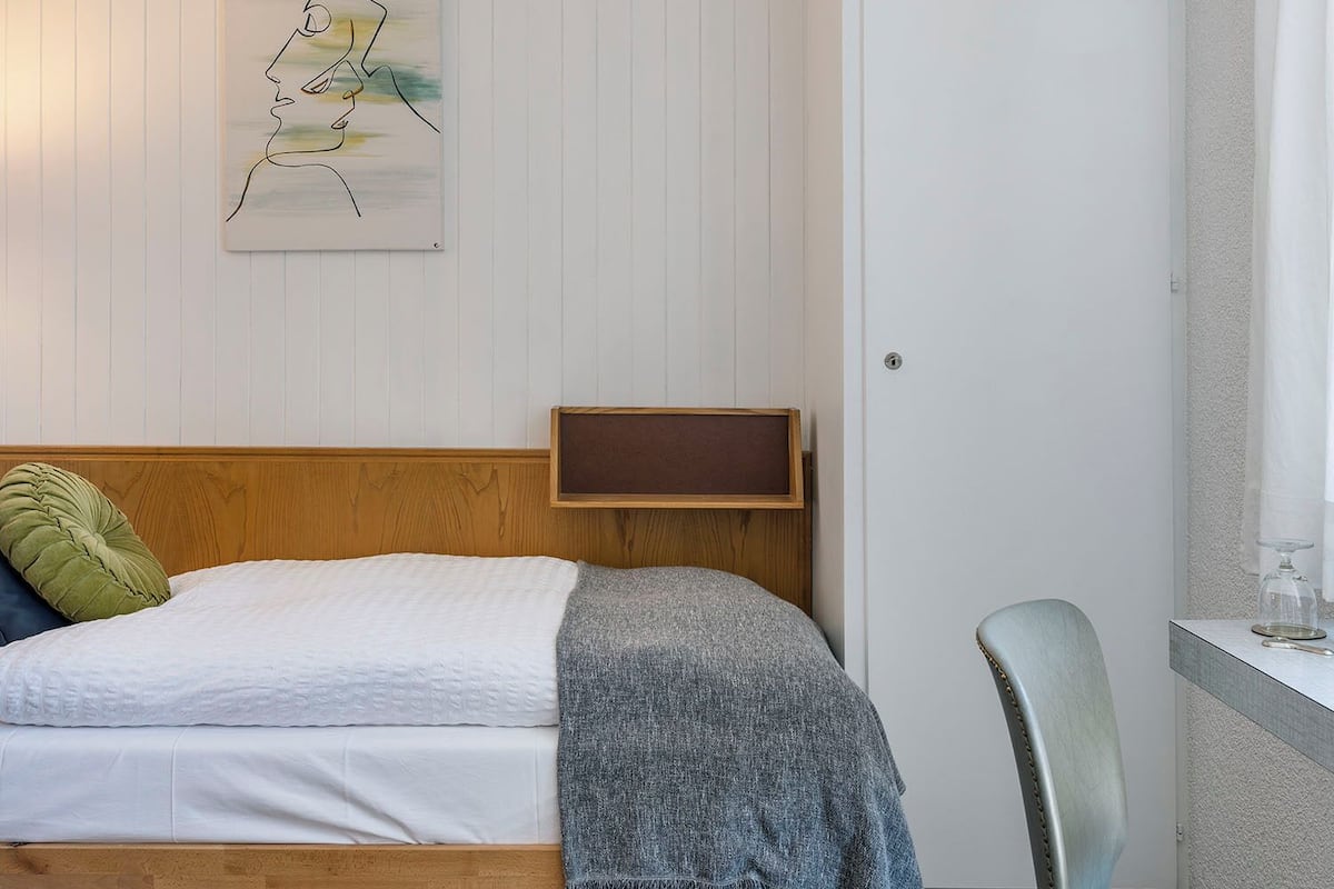 Une chambre à coucher avec un lit en bois, une tête de lit, une table de chevet, une chaise, un tapis et une œuvre d’art accrochée au mur.
