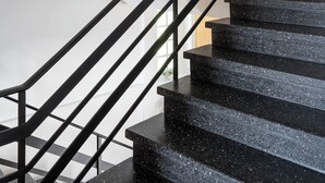A modern staircase with black metal railings and black granite steps, leading to a wooden wall with a round mirror.