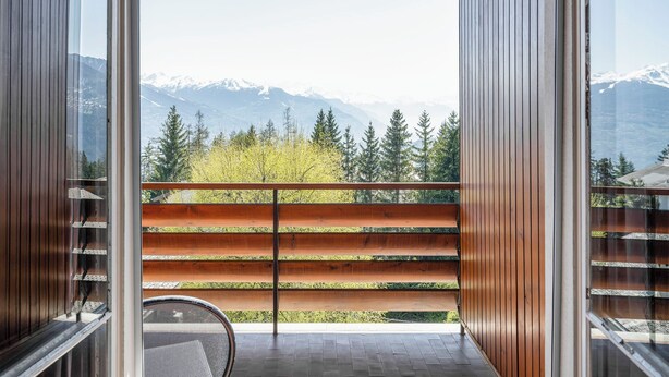 A balcony with a wooden railing overlooking a mountainous landscape.