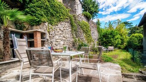 Un patio al aire libre con suelo de piedra, mobiliario de mimbre y una pared de piedra cubierta de follaje.