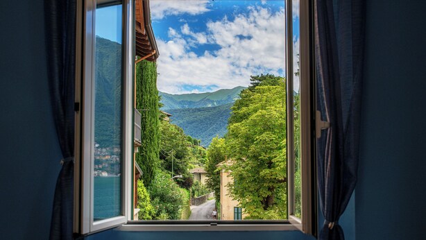 Ventana con vista a un paisaje montañoso, una carretera y vegetación.
