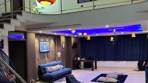 A modern living room with a blue sofa, black bean bag chairs, and a TV on the wall. - Area 369 (Jaipur)