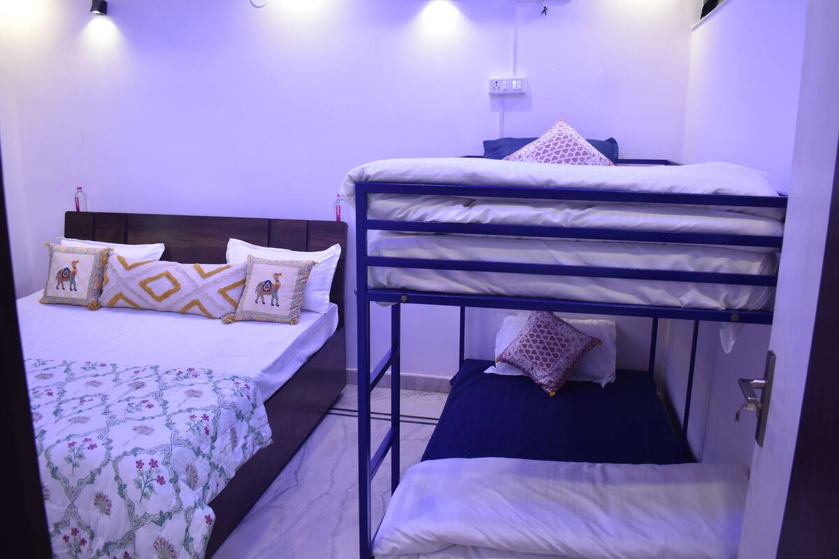 A room with a bunk bed and a single bed, both with white bedding and patterned pillows.