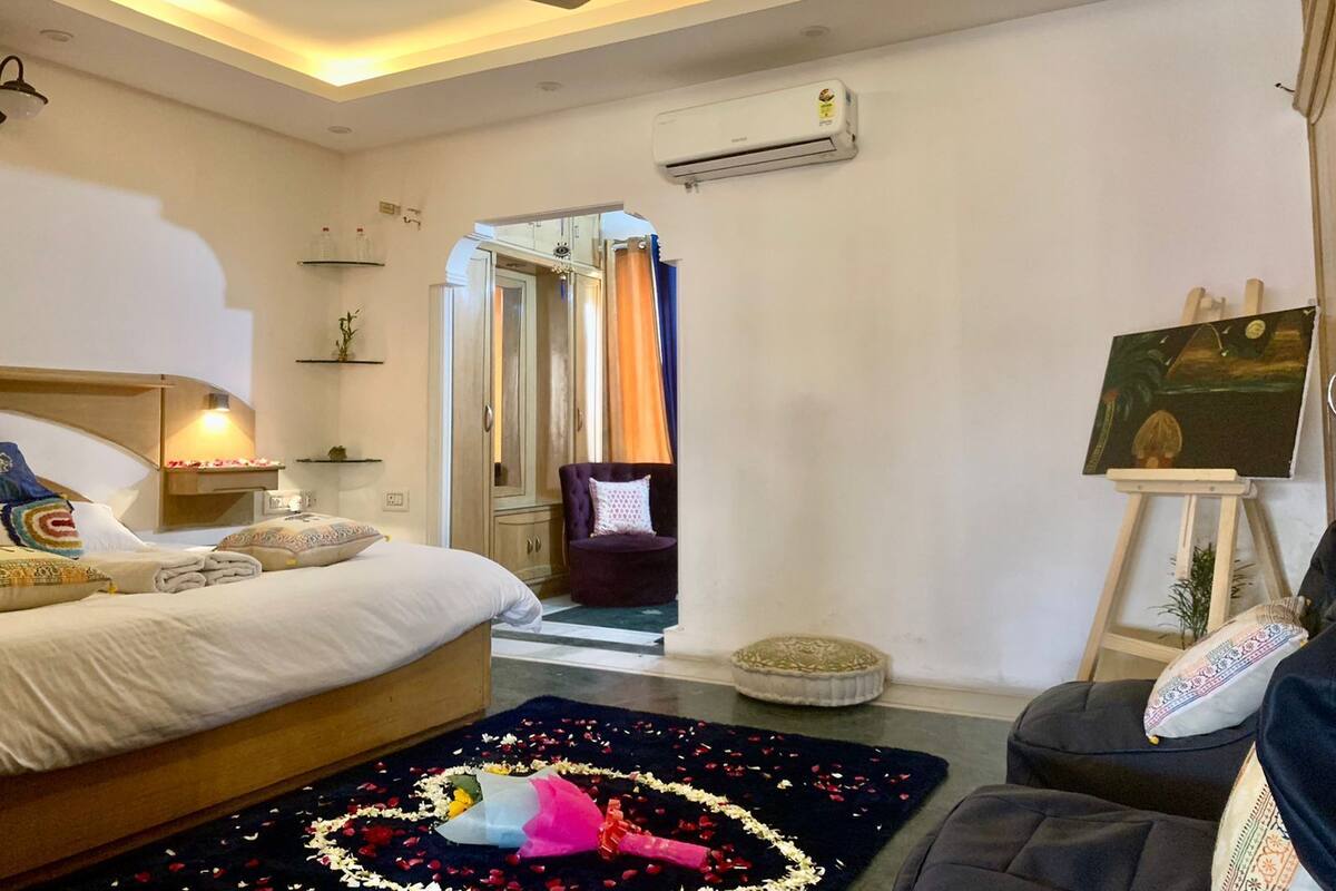 A bedroom with a bed, a chair, an easel with a painting, and a ceiling fan.
