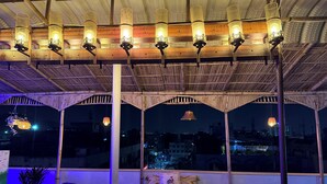 A rooftop terrace with a bed, chairs, and hanging lanterns. - Area 369 (Jaipur)