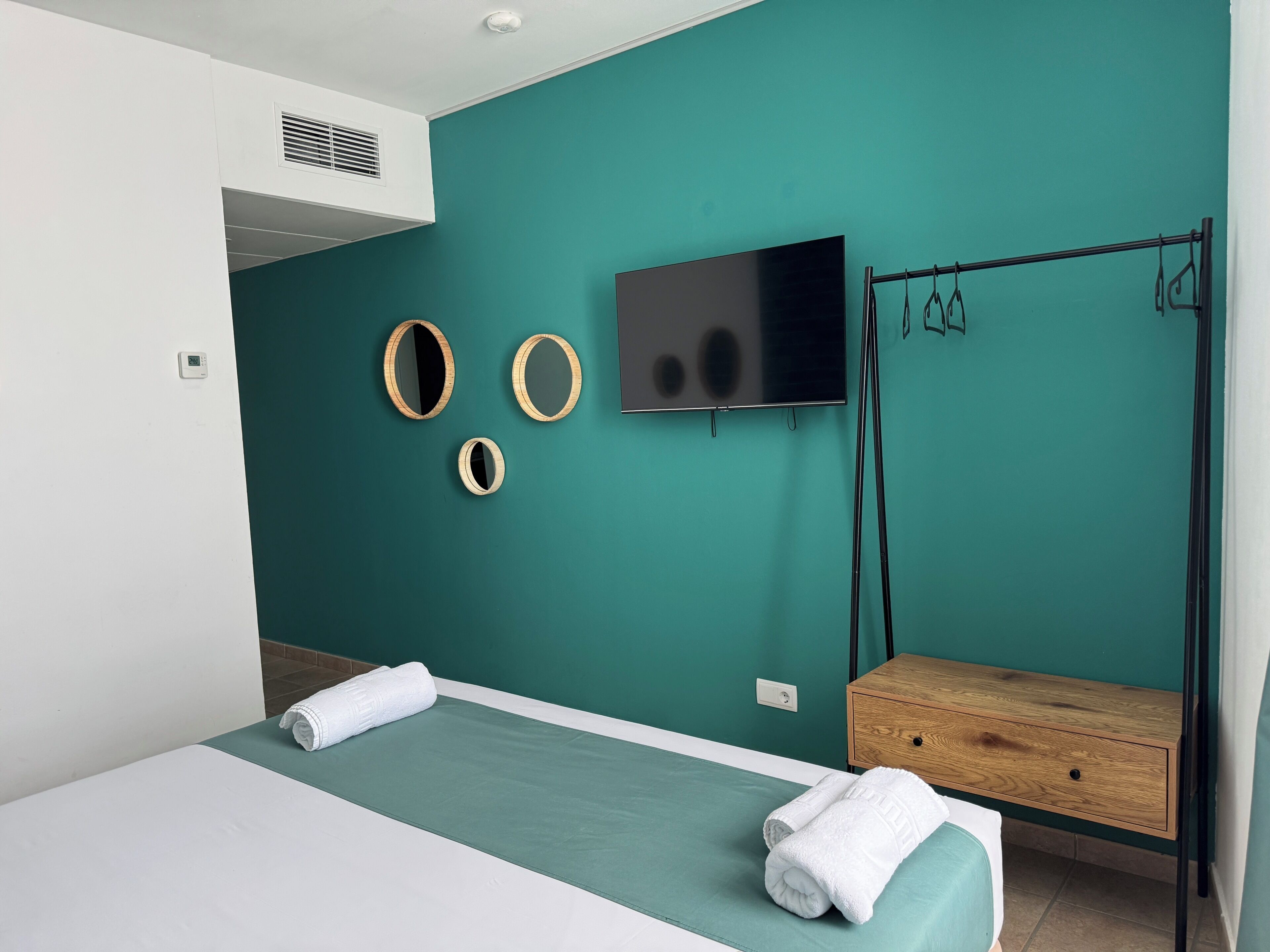 Un dormitorio moderno con paredes verde azulado, una cama con ropa de cama blanca, un televisor y una mesita de noche de madera.
