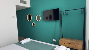 Un dormitorio moderno con paredes verde azulado, una cama con ropa de cama blanca, un televisor y una mesita de noche de madera.