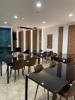 Un salón de conferencias con varias mesas y sillas, una pantalla grande y una pared decorativa de ladrillo.