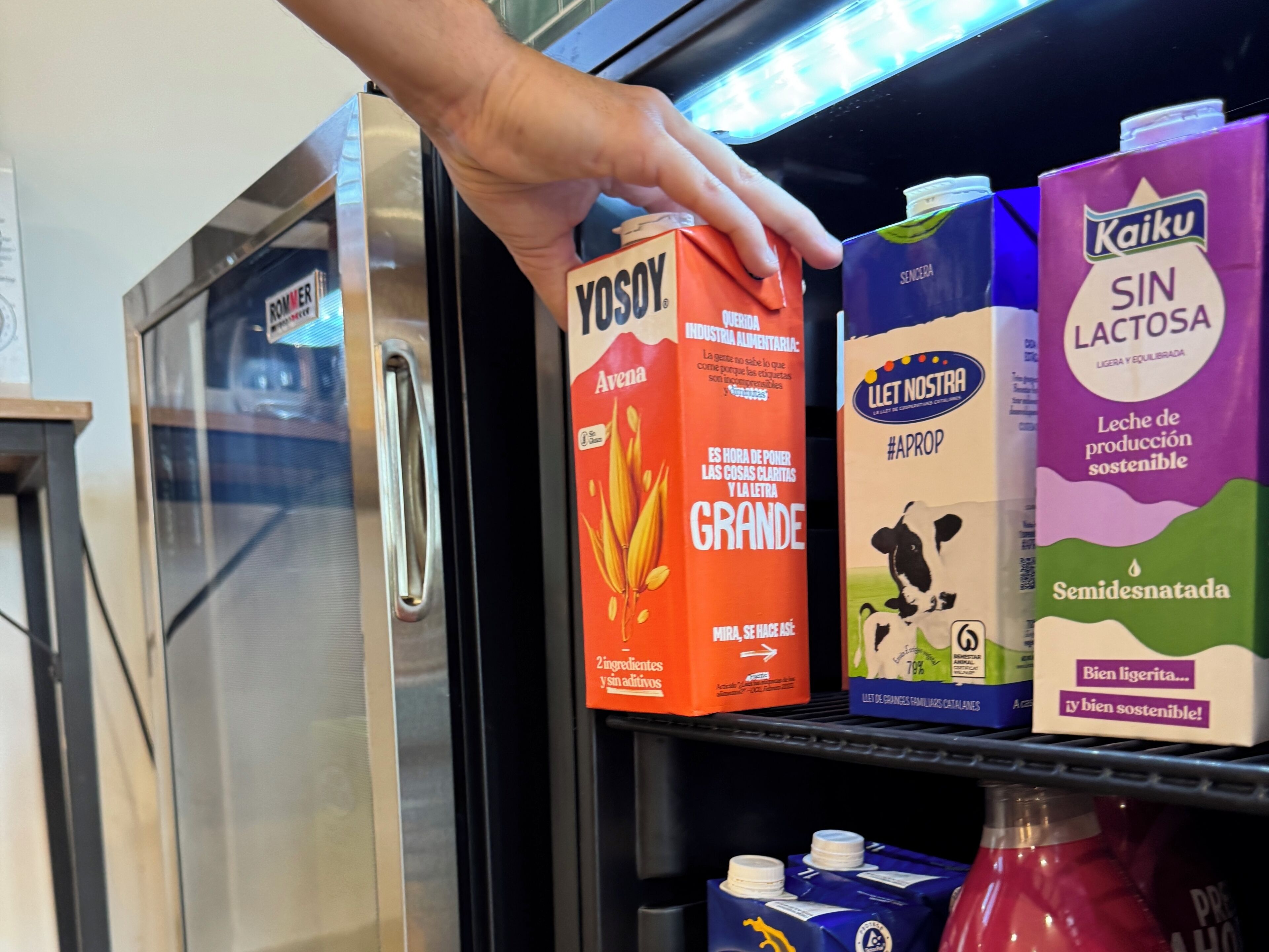 A hand reaching for a carton of VOSOY milk on a shelf.