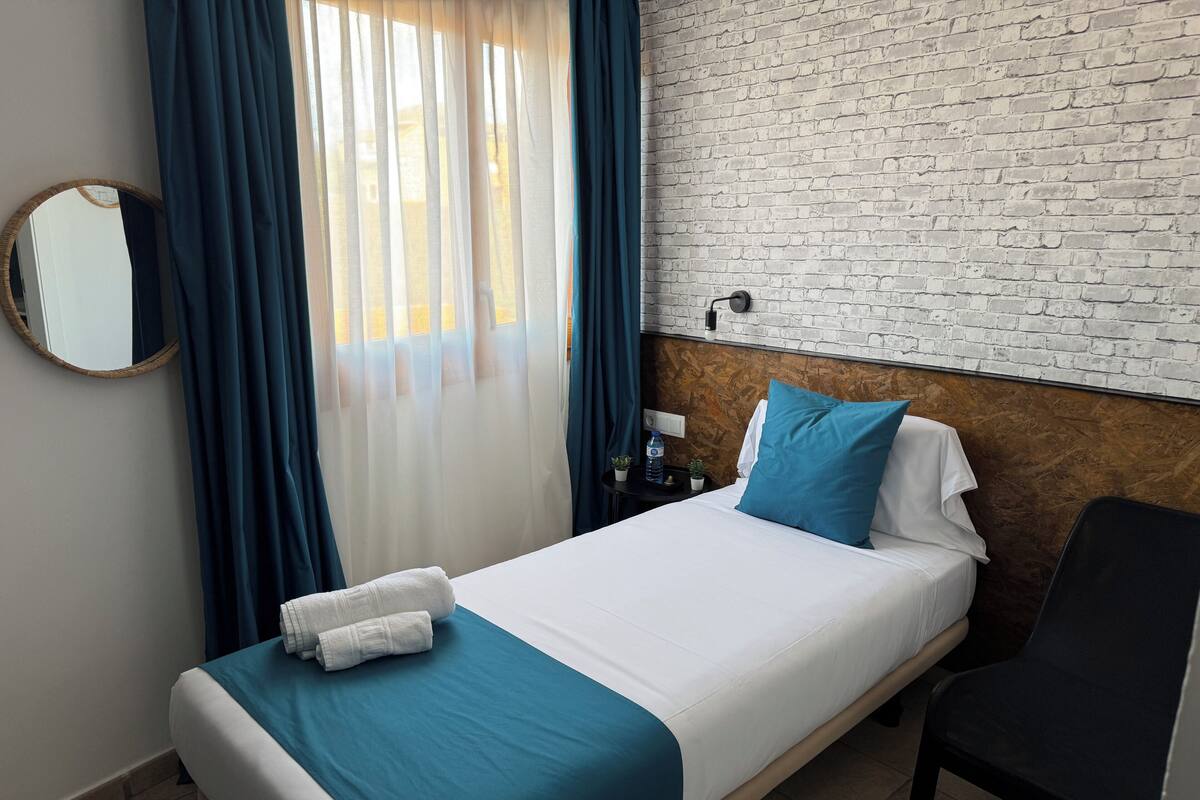 Ein Hotelzimmer mit Bett, Stuhl, Spiegel, Nachttisch und einer Wand mit Ziegelmuster.