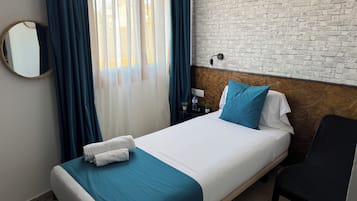 Habitación de hotel con cama, una silla, un espejo, una mesita de noche y una pared con diseño de ladrillos.