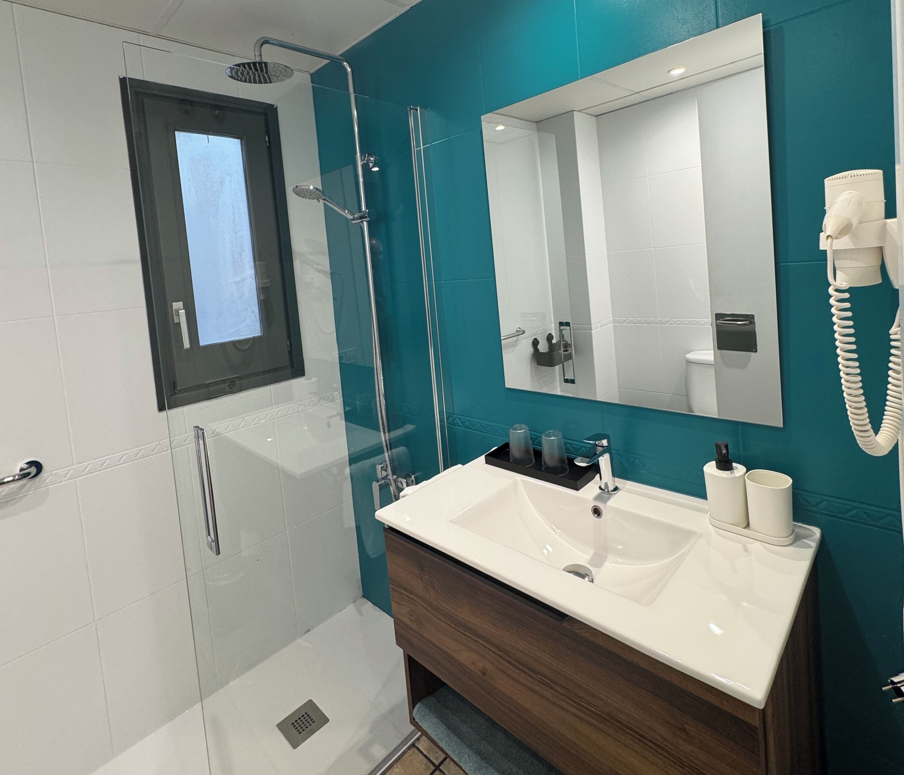 Un baño moderno con ducha de vidrio, un espejo grande y un tocador con lavamanos y toallero.