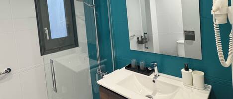 Un baño moderno con ducha de vidrio, un espejo grande y un tocador con lavamanos y toallero.