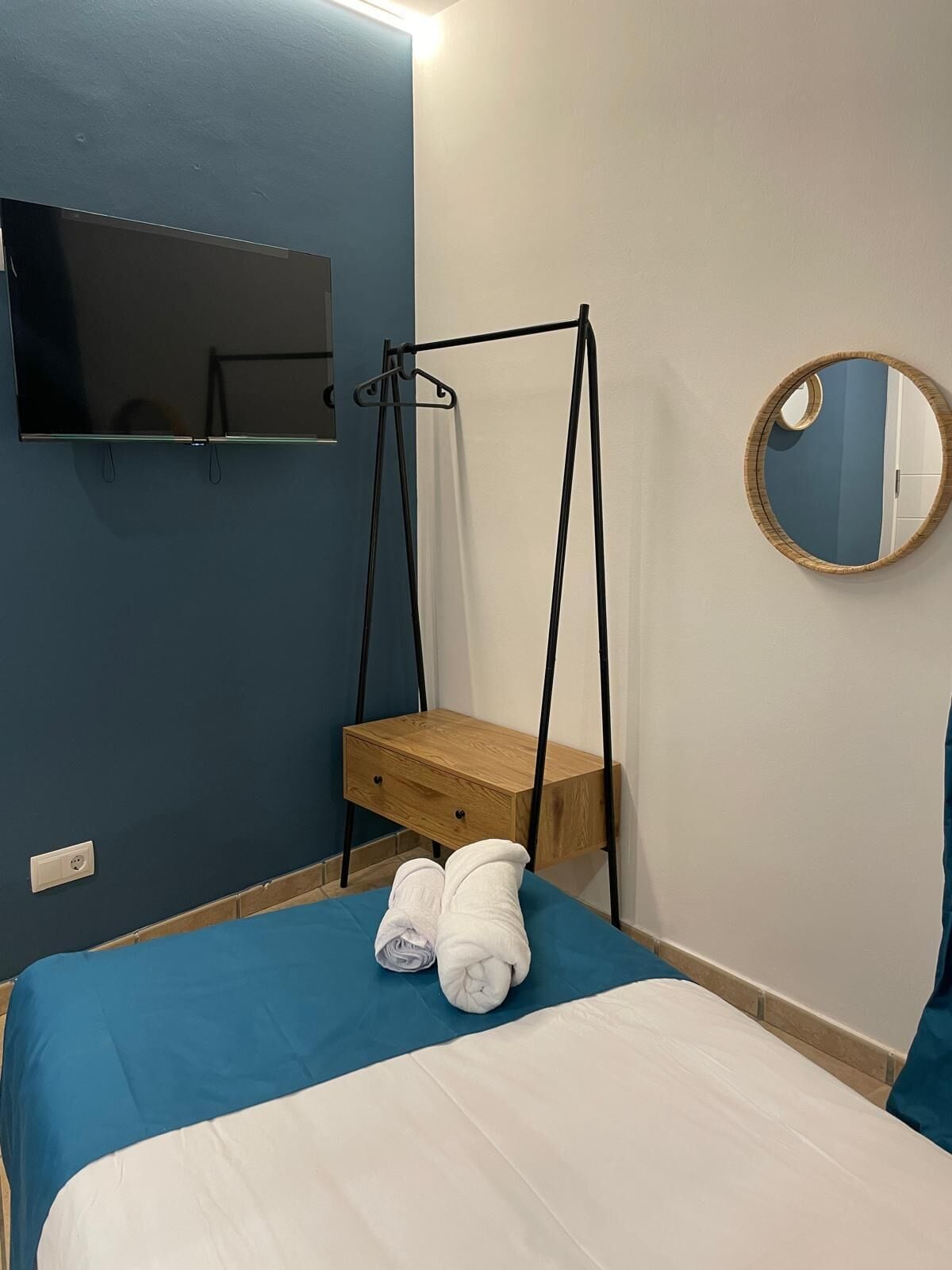 A bedroom with a bed, a hanging chair, a bedside table, a mirror, and a wall-mounted TV.