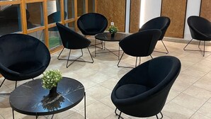 Un intérieur moderne avec des chaises noires et une petite table agrémentée d’une plante, de grandes fenêtres et un téléviseur à écran plat fixé au mur.