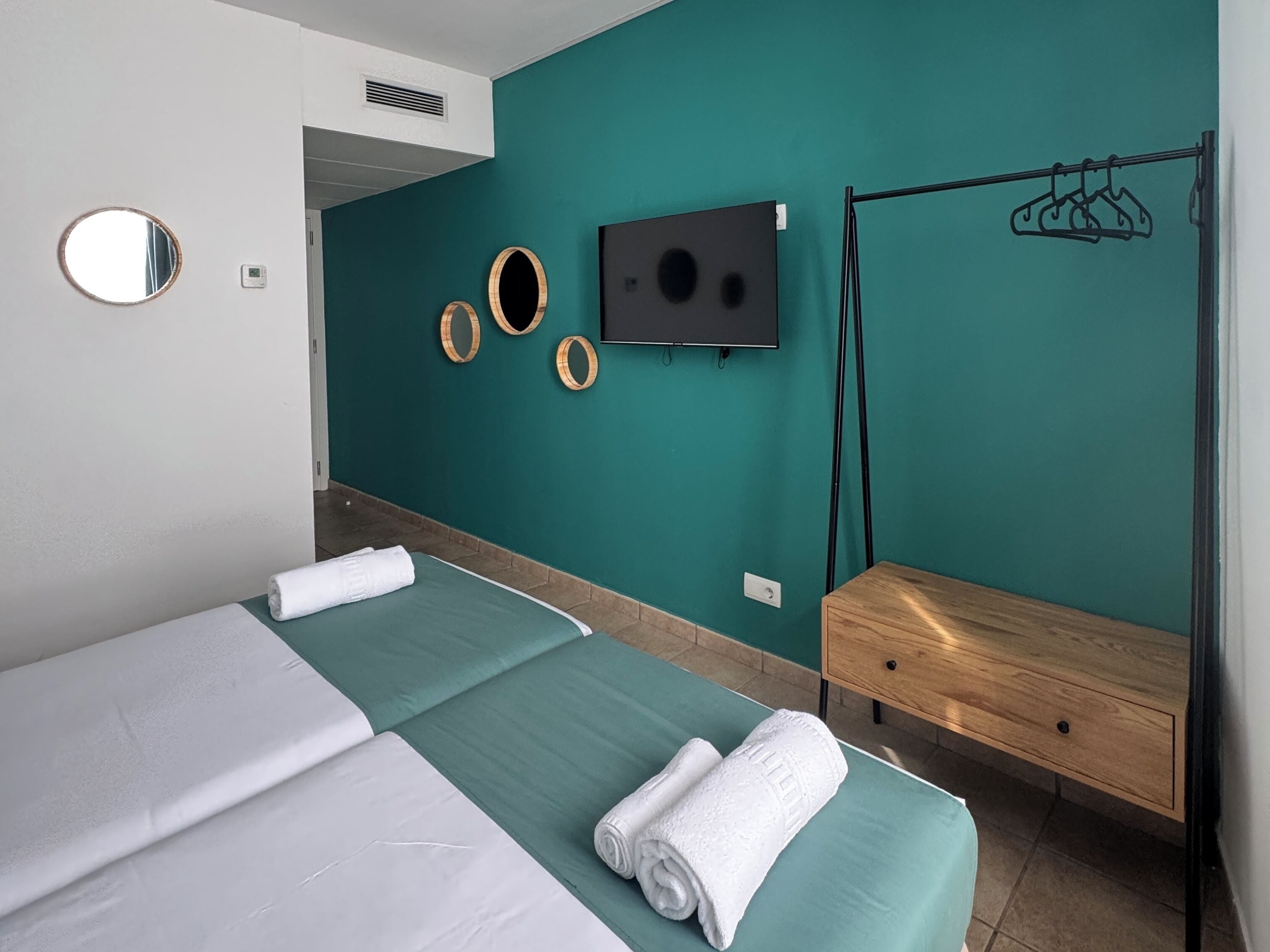 Une chambre d’hôtel avec deux lits, une télévision, un miroir et une table de chevet en bois.