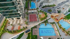 Un immeuble de grande hauteur doté de nombreux balcons, d’un terrain de basketball et d’une piscine.