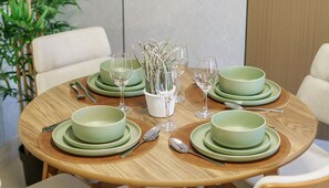 Une table ronde en bois, dressée avec de la vaisselle verte : assiettes, bols et verres à vin, ainsi que des couverts en argent.