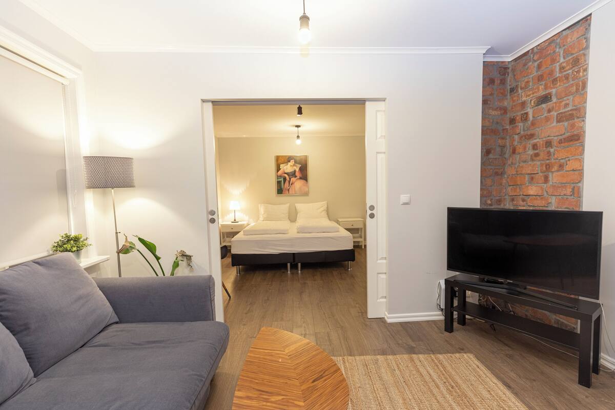A modern living room with a grey sofa, a wooden coffee table, a flat-screen TV on a black stand, and a brick wall.
