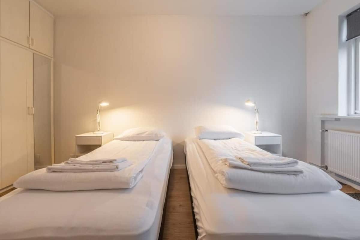A twin room with two beds, each with a bedside table and lamp, and a wardrobe on the left.