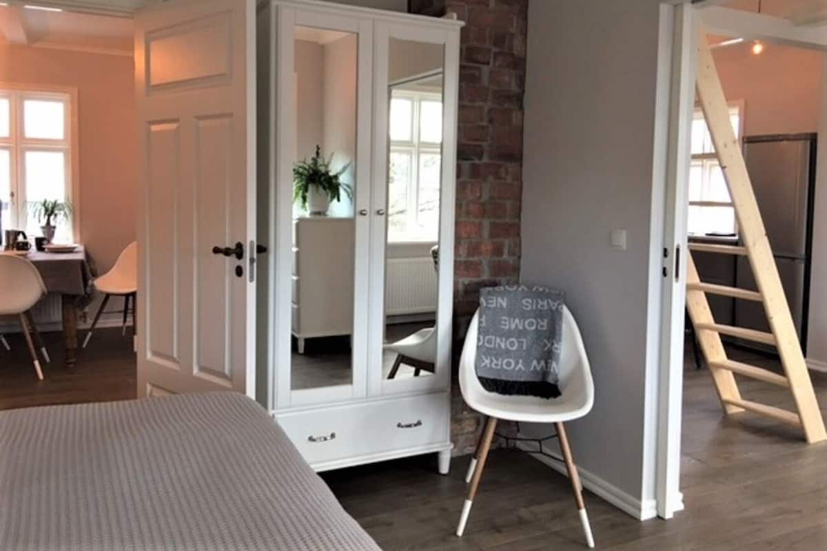 A bedroom with a bed, a wardrobe, a chair, and a staircase.