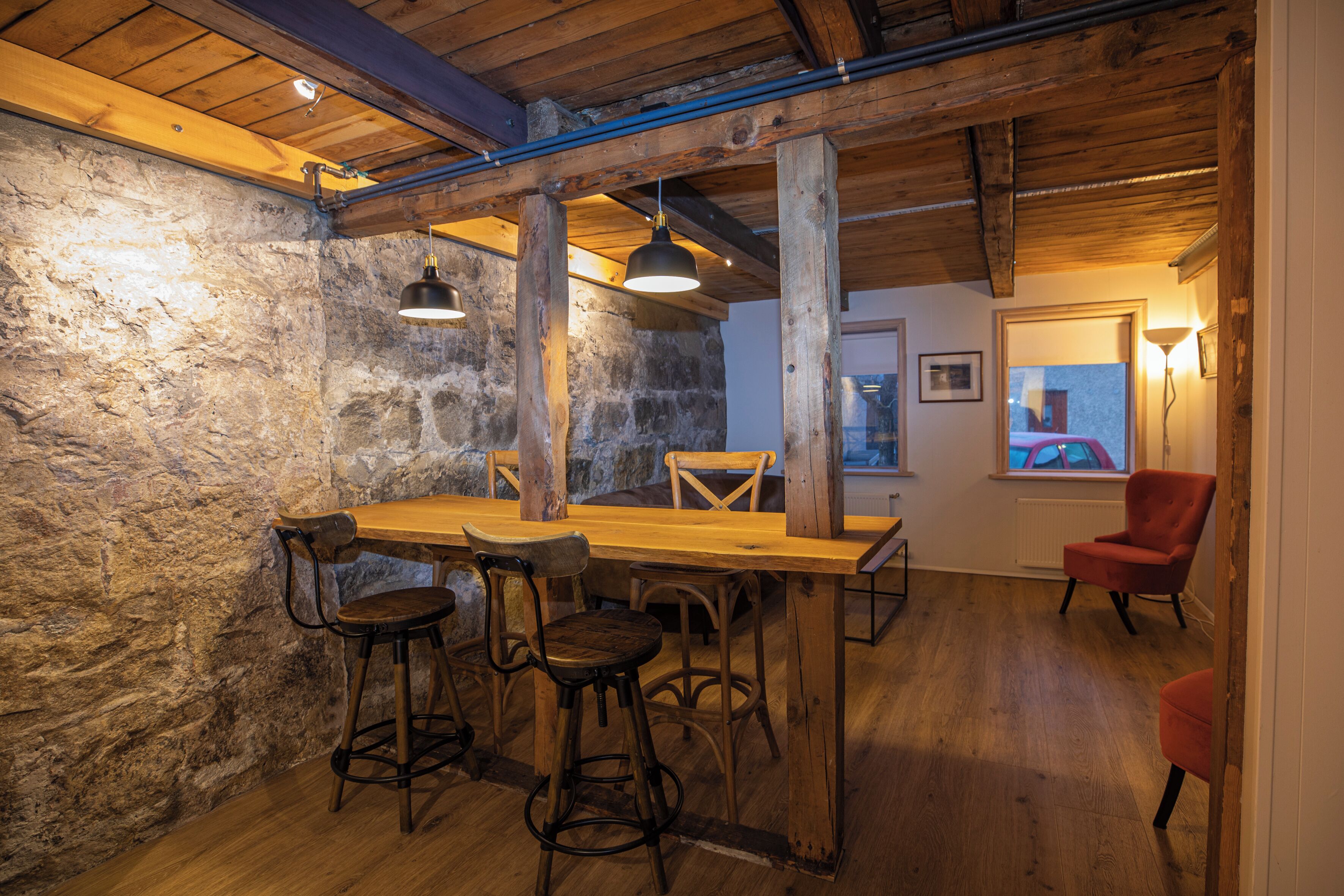 Ein rustikales Interieur mit freiliegenden Holzbalken, einer Steinwand und einem Holzesstisch mit Barhocker.