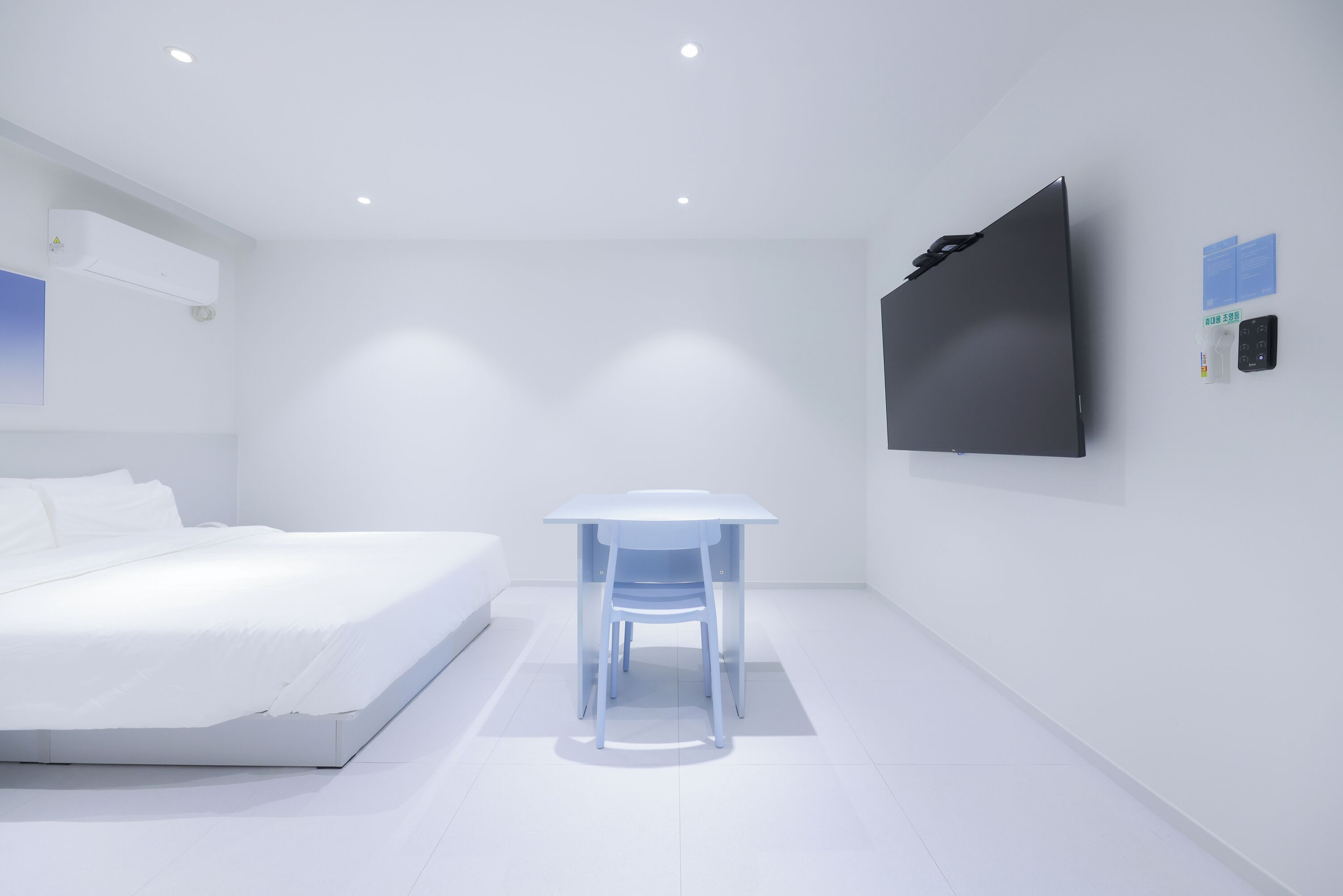 A modern bedroom with a bed, a small table, and a wall-mounted TV.