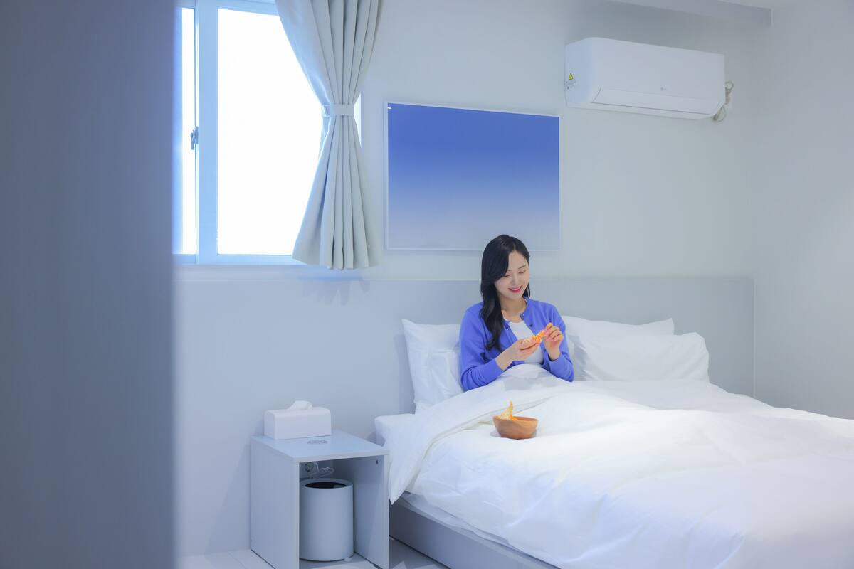 A hotel room with a bed, a nightstand, a trash bin, and a window with curtains.