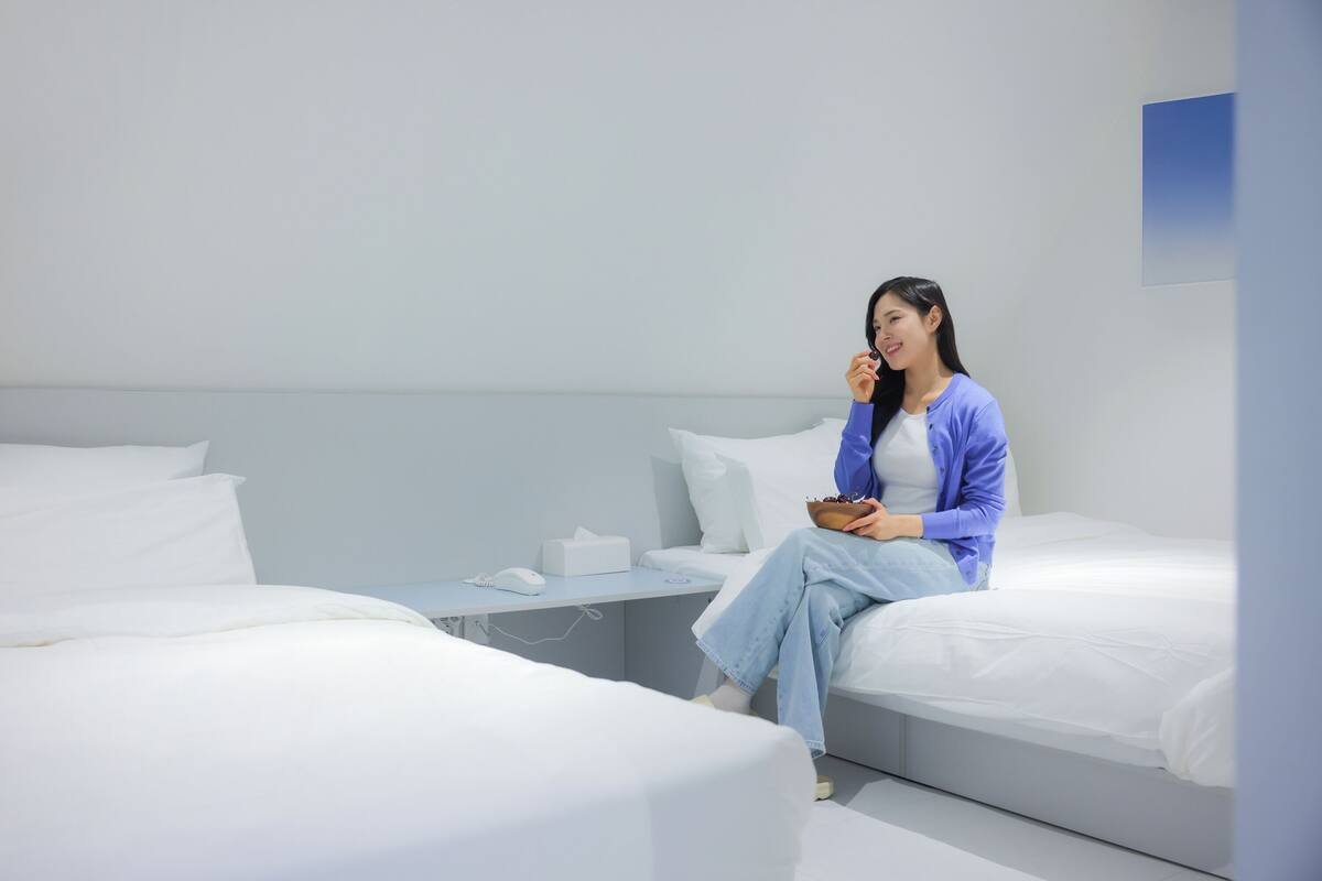 A hotel room with two beds, a bedside table with a phone and tissues, and a wall-mounted light fixture.
