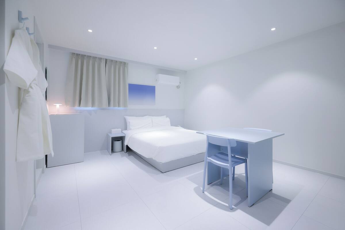 A modern hotel room with a bed, bedside table, and a desk with a chair.