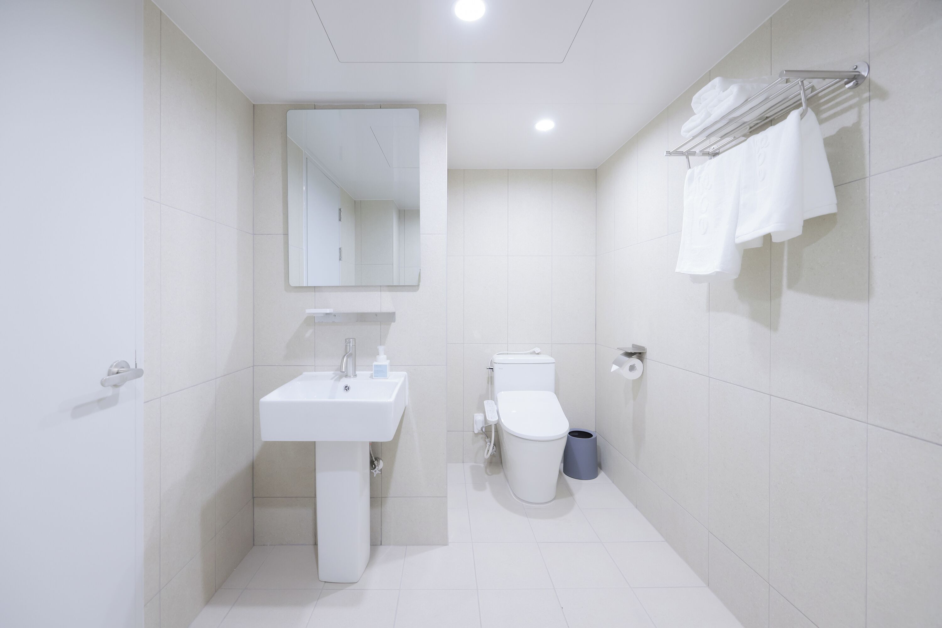 Et moderne badeværelse med vask, spejl, toilet og håndklæderække.