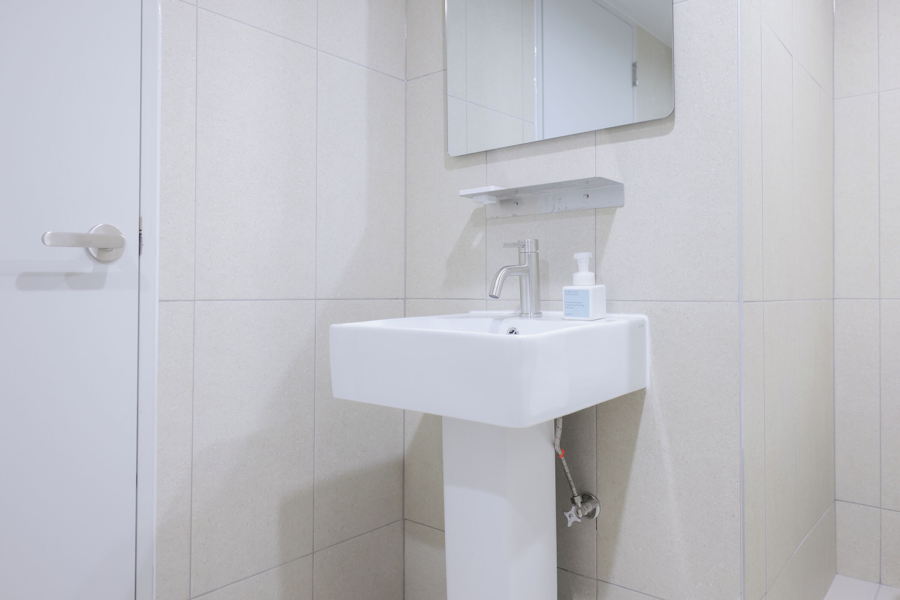 A bathroom with a white sink, a mirror above it, and a door to the left.