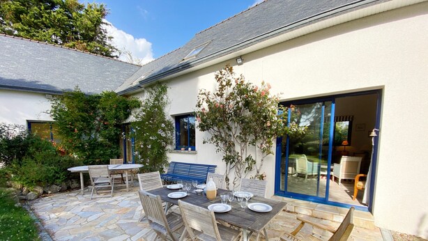 A patio with stone flooring, a wooden table set for dining, and a blue bench.