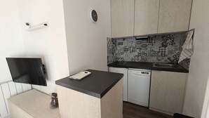 A compact kitchen with a built-in dishwasher, a small island with a sink, and a wall-mounted clock. - Modern 1-bedroom apartment with pool, near skiing and village (Arêches-Beaufort)