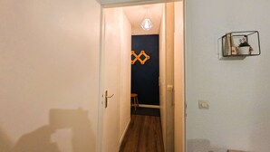 A hallway with a wooden floor, a door leading to a room with a dark wall and a geometric decoration, and a small shelf with a plant and a star decoration. - Modern 1-bedroom apartment with pool, near skiing and village (Arêches-Beaufort)