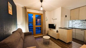 A living room with a sofa, a TV, a small round table, and a kitchen area with cabinets and a countertop. - Modern 1-bedroom apartment with pool, near skiing and village (Arêches-Beaufort)
